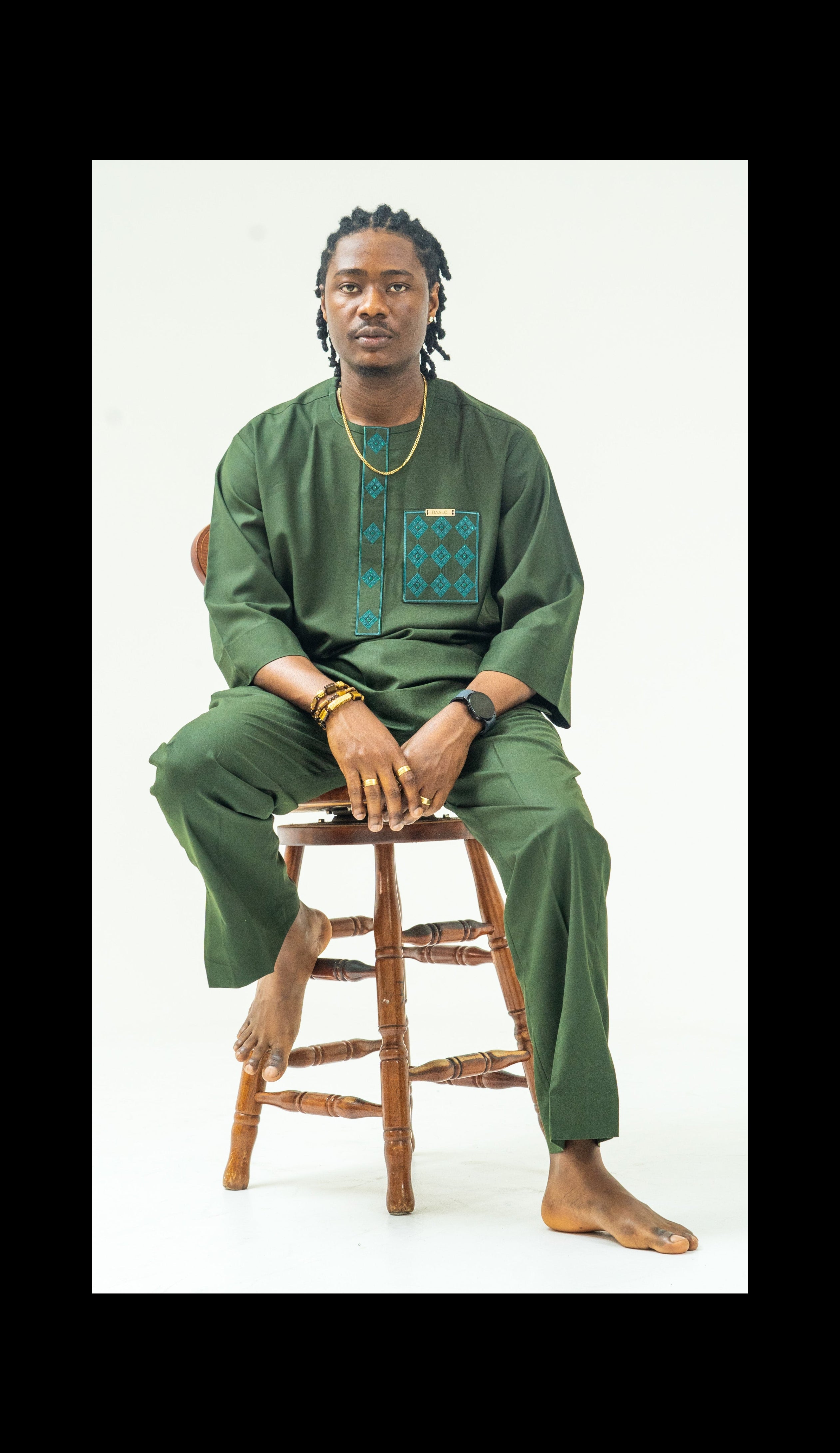 Person wearing a green traditional outfit sitting on a wooden stool against a white background