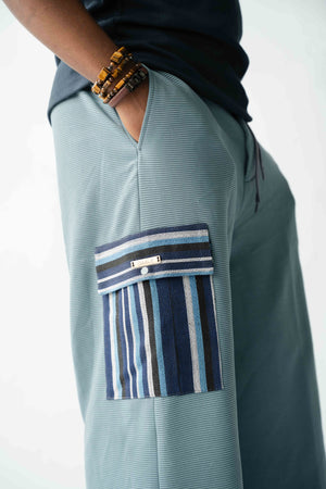 Luxury pale blue wide-leg cargo trousers for men featuring handcrafted blue Aso Oke cargo pockets, premium textured fabric, drawstring waist and contemporary African-inspired design. Designed in London for modern statement menswear.
