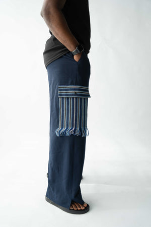 Navy wide-leg men's cargo trousers with handwoven Aso Oke pocket detail and fringe trim, side profile view.