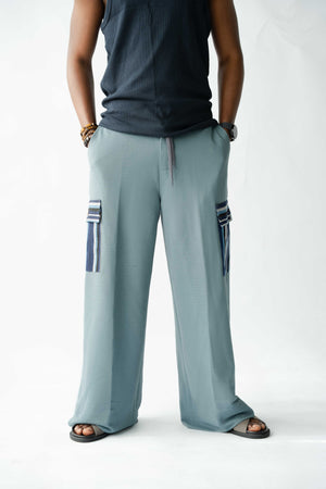 Contemporary African-inspired pale blue cargo trousers featuring handcrafted woven Aso Oke pocket detailing and relaxed silhouette.