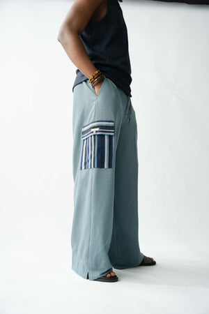 Pale blue wide-leg cargo trousers for men featuring handcrafted striped Aso Oke pocket detail, side profile view.