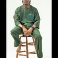 Person wearing a green traditional outfit sitting on a wooden stool against a white background