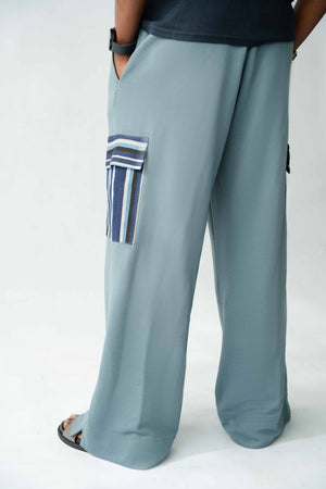 Contemporary African-inspired pale blue cargo trousers featuring handcrafted woven Aso Oke pocket detailing and relaxed silhouette.