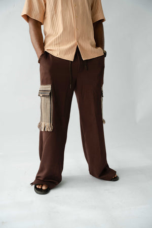 Brown wide-leg cargo trousers for men featuring handcrafted Aso Oke cargo pockets with fringe detailing, front view.