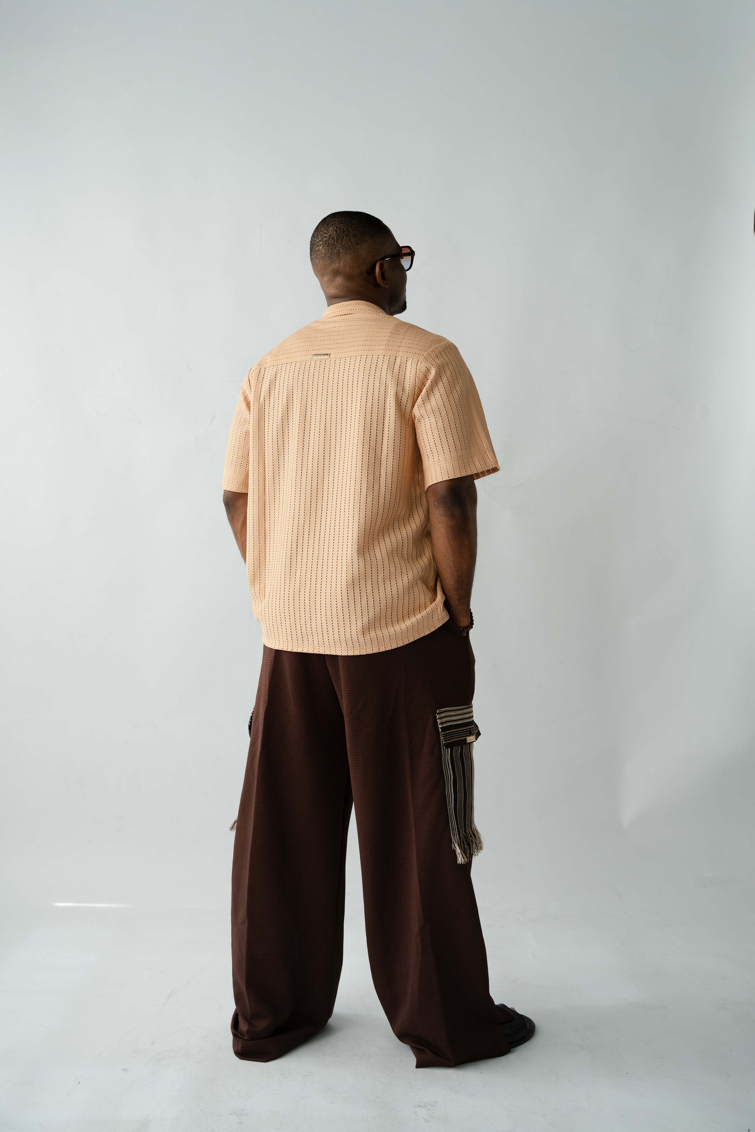 Brown textured wide-leg trousers with oversized silhouette, drawstring waist and traditional Aso Oke cargo pockets.
