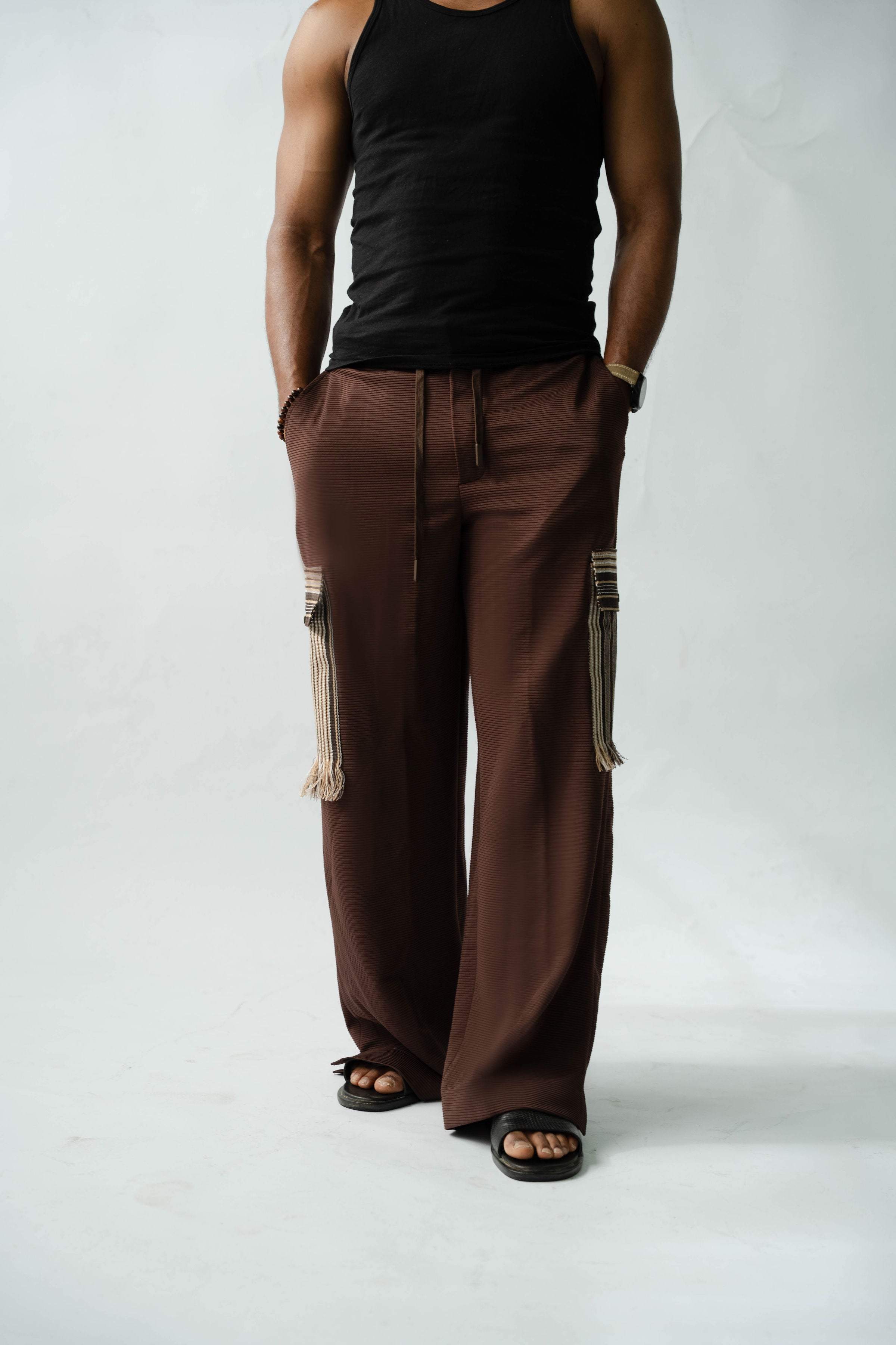 Designer brown cargo trousers featuring artisan woven Aso Oke pocket details and relaxed premium tailoring.