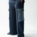 Navy wide-leg men's cargo trousers with handwoven Aso Oke pocket detail and fringe trim, side profile view.